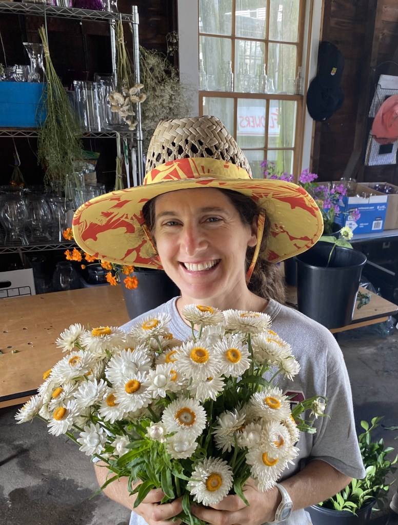 Syrah wearing a colorful sun hat and holding a bouquet of white flowers